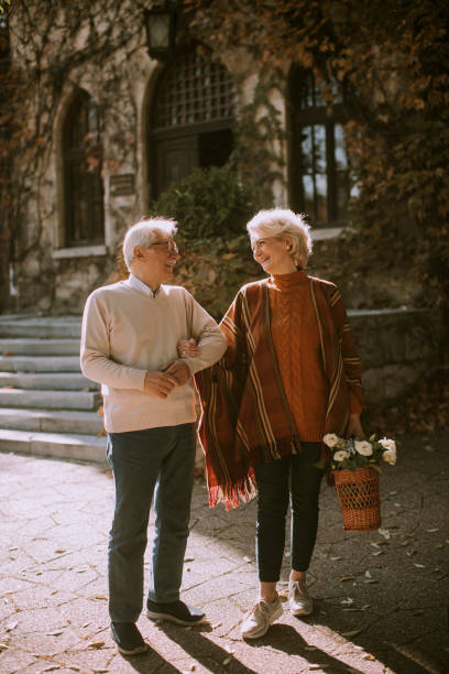 pareja de ancianos caminando con canasta llena de flores y comestibles en el parque de otoño - senior adult mature adult senior couple heterosexual couple fotografías e imágenes de stock