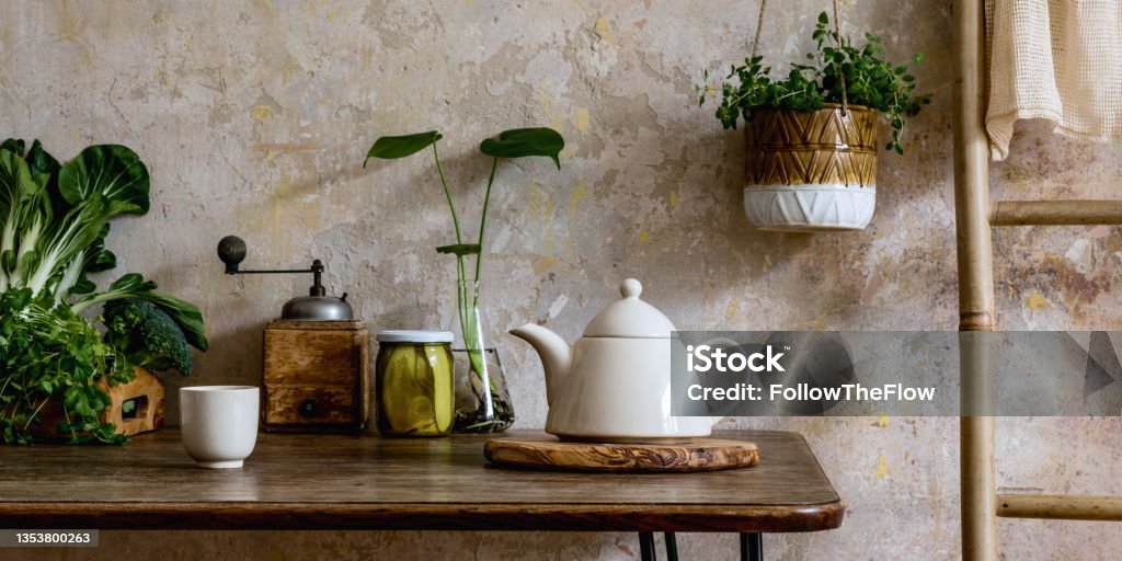 Stylish composition of kitchen interior with wooden mock up frame, family table, ladder, vegetables, tea pot, dessert and kitchen accessories. Wabi sabi concept of home decor. Country side. Template. Stylish composition of kitchen interior and kitchen accessories. Wabi sabi concept of home decor. Template. Apartment Stock Photo