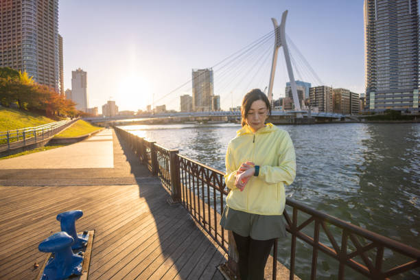 Japanese woman using smart watch during jogging at riverside