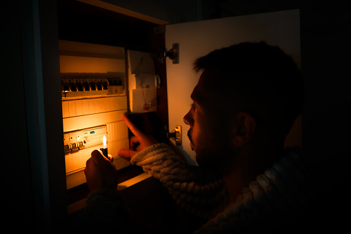 Hombre con encendedor en la oscuridad total investigando la caja de fusibles o la centralita eléctrica en casa durante el corte de energía. Apagón, sin concepto de electricidad photo