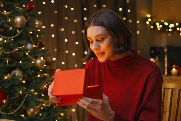 istock A pretty girl is opening a gift box and a magic light from it illuminates her face, she is sitting at home in a Christmas Eve 1353803930