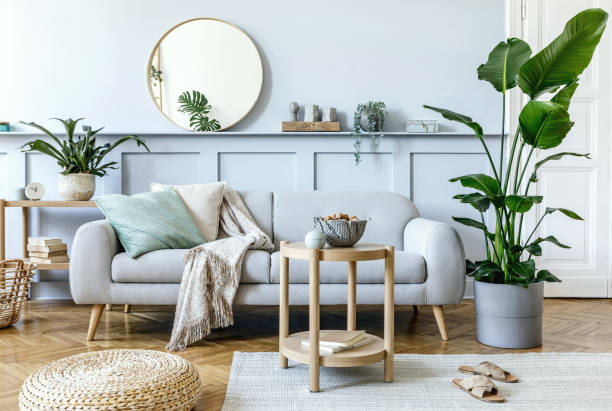 istock Stylish living room interior with design grey sofa, coffe table, pouf, basket, shelf, mirror, tropical plants, decoration, carpet, pillows and elegant personal accessories in modern home decor. 1353806015