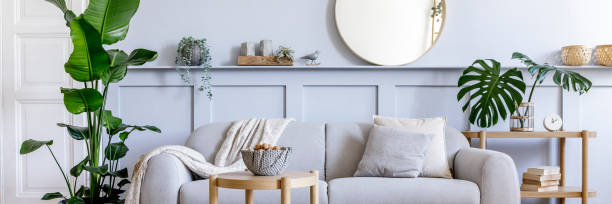 istock Stylish living room interior with design grey sofa, coffe table, pouf, basket, shelf, mirror, tropical plants, decoration, carpet, pillows and elegant personal accessories in modern home decor. 1353806087