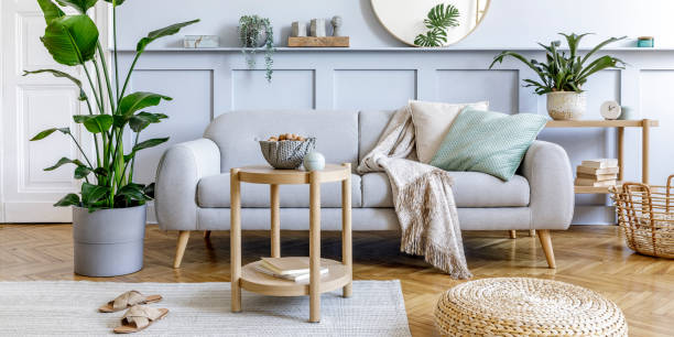 istock Stylish living room interior with design grey sofa, coffe table, pouf, basket, shelf, mirror, tropical plants, decoration, carpet, pillows and elegant personal accessories in modern home decor. 1353806119