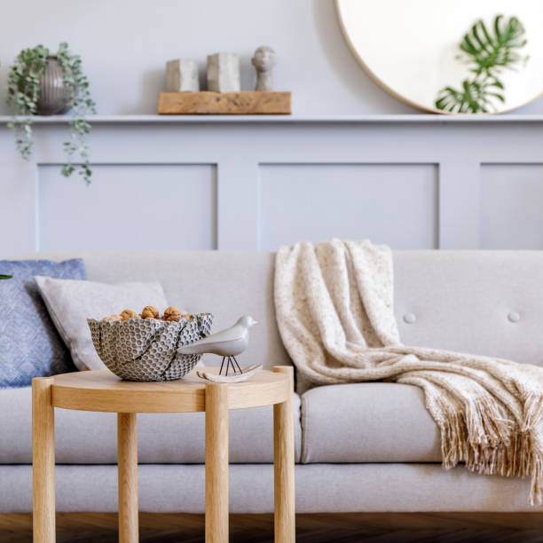 istock Stylish living room interior with design grey sofa, coffe table, pouf, basket, shelf, mirror, tropical plants, decoration, carpet, pillows and elegant personal accessories in modern home decor. 1353806127