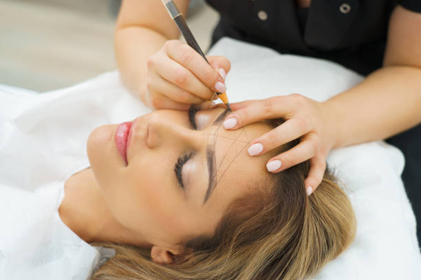 Permanent Makeup For Eyebrows. Microblading brow. Beautician Doing Eyebrow Tattooing For Female Face. Beautiful young girl in a beauty salon stock photo