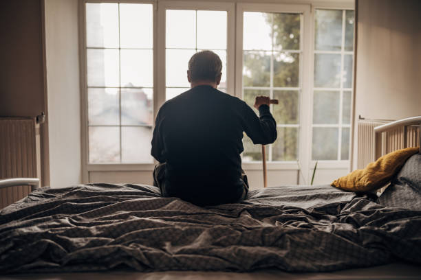 ein einsamer mann sitzt auf dem bett - altersheim stock-fotos und bilder