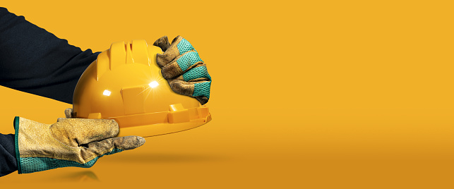 Manos con guantes de trabajo protectores que sostienen un casco de seguridad amarillo photo