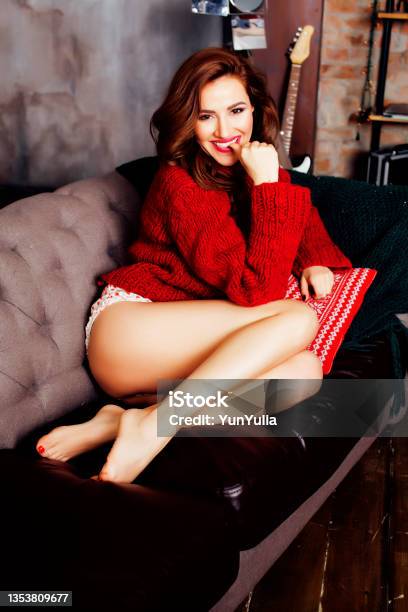 Young Pretty Stylish Woman In Red Winter Sweater At Couch In Home Interior Happy Smiling Lifestyle People Concept Stock Photo - Download Image Now