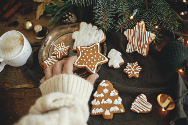 istock Hand holding gingerbread cookie star on rustic table with coffee and fir branches. Happy Holidays 1353814756