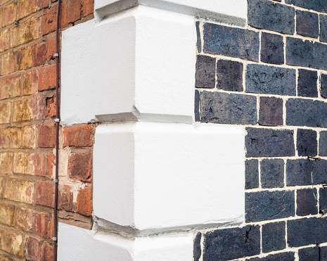 A close-up of the corner of a traditional English apartment building, with differently finished bricks and white painted corner stones.