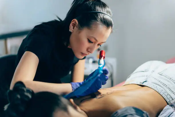 Tattoo artist drawing new tattoo on woman’s back