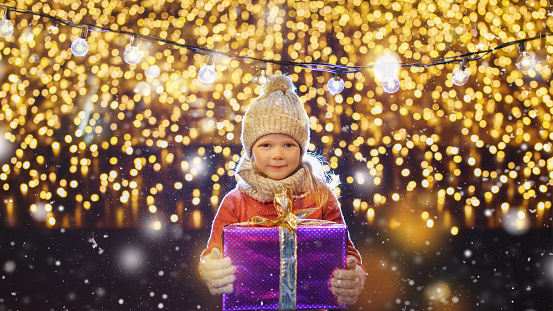 holidays, childhood and people concept - happy little girl with gift box at christmas market in winter evening
