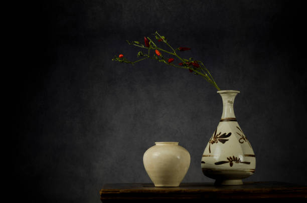 bodegón de porcelanas antiguas chinas, un jarrón en forma de pera y un frasco blanco, con rama de chiles rojos sobre mesa de madera sobre fondo gris - buddhist puja fotografías e imágenes de stock