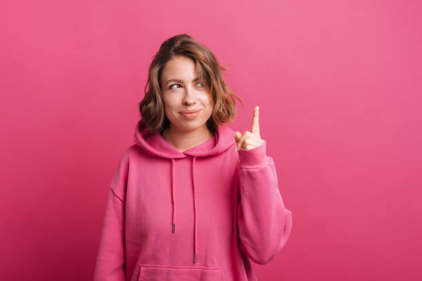 Portrait of beautiful young trendy woman in pink hoodie pointing up with finger stock photo