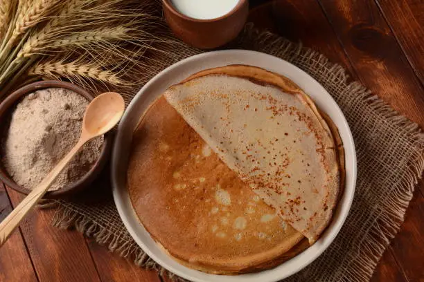 A traditional French Savory Buckwheat Galettes Bretonnes pancakes on a table with  flour, wheat plant and milk