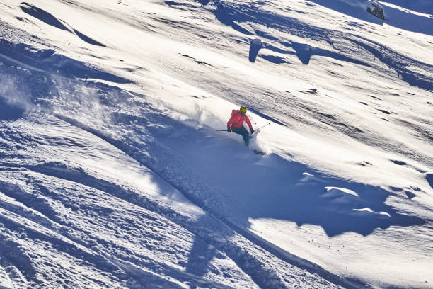 istock Skier descends snowy mountain ridge, in the sunshine 1353837676