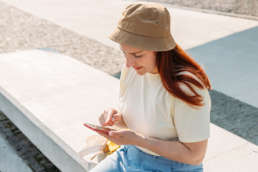 Close-up image of young hipster girl using modern smartphone device outdoors, female hands typing text message via cellphone