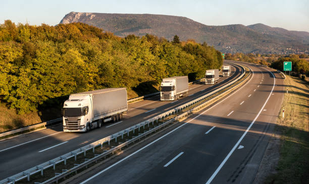 Transit photo - Convoy of transportation trucks Convoy or caravan of transportation trucks passing on a highway at sunset. Highway transit transportation with red and yellow lorry trucks auto shipping stock pictures, royalty-free photos & images