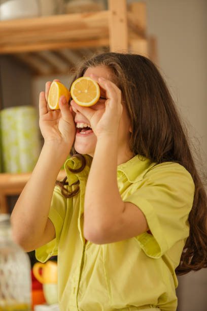 istock Cheerful young girl putting lemons as her eyes while playing and having fun 1353848310