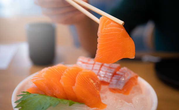 istock Using chopsticks, salmon sashimi. Sashimi is a popular dish of Japanese restaurants. 1353849138