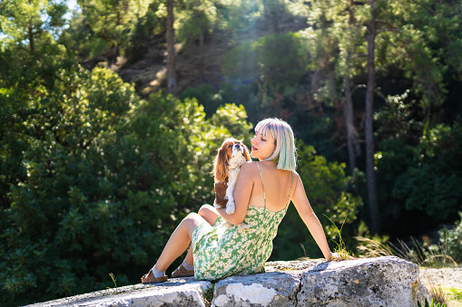 Image of a young woman with colorful hair and her dog sitting in front of forest landscape