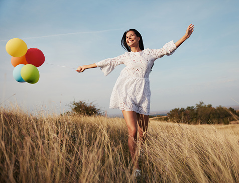 Happy young girl running with balloons through meadow grass
