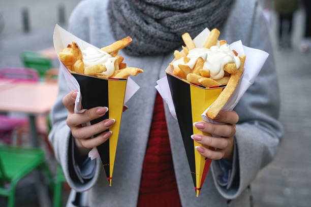 Belgian frites or french fries with mayonnaise in Brussels, Belgium. Female tourist holds two portions of fries in hands in the street. stock photo