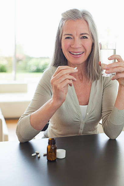 lächelnd frau holding glas wasser und tabletten schlucken - hove stock-fotos und bilder