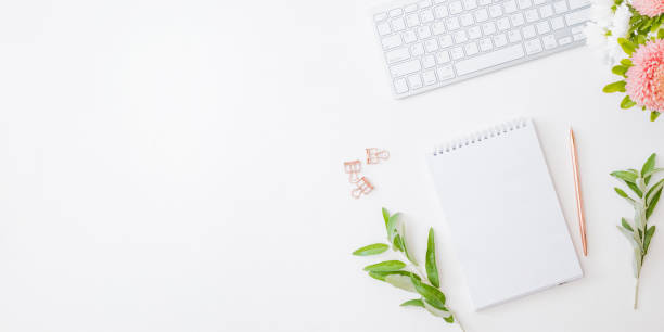 istock Flat lay home office desktop with notebook, flowers in a vase, office supplies on a light background 1353855406
