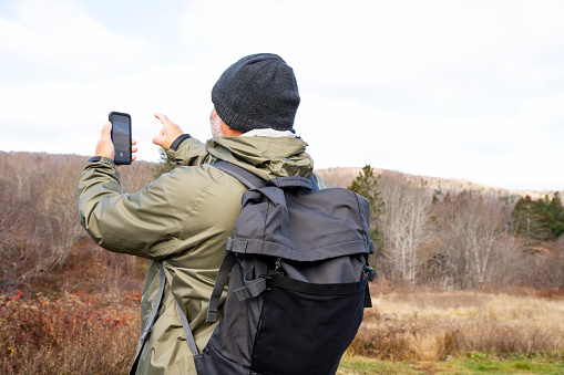 A man using a smartphone while on hike on a cold day in the winter. Photographed in North America.