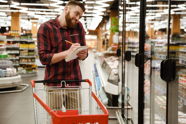 istock Cheerful young man in supermarket talking by phone writing notes 1353860613