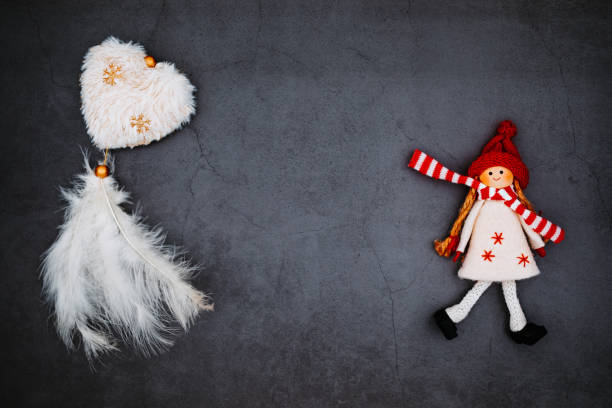 istock Flat lay Christmas card with dark background marbled effect, a white plush heart with feathers and a smiling christmas wooden doll with winter scarf 1353863735