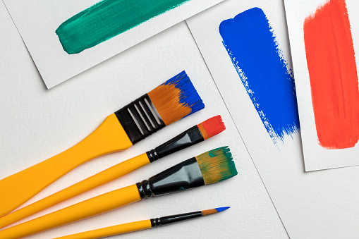 Set of paintbrushes with multi colored strokes on white paper sheets.
