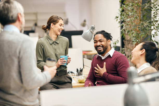 Happy business team having fun while talking on their coffee break in the office. Multi-ethnic group of entrepreneurs laughing while talking to each other on a break in the office. coffee break stock pictures, royalty-free photos & images