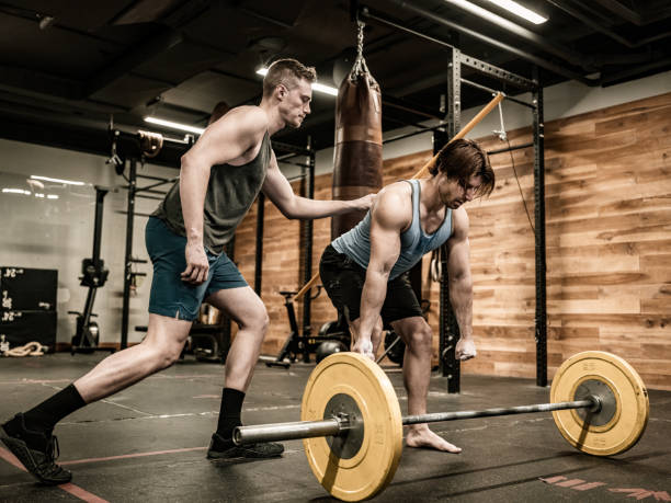 istock Young Man lifting weights with his trainer in the Gym 1353874073