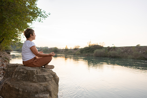 Beautiful spiritual woman meditating by the lake, wearing beige clothes