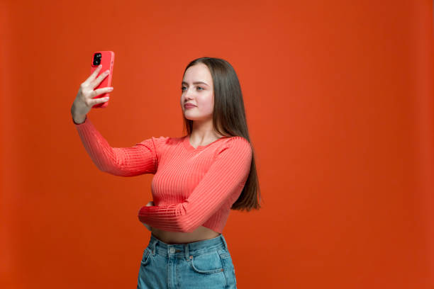 istock Pretty young girl looking at phone using mobile camera or apps taking selfie for social networks content, blogging 1353874355