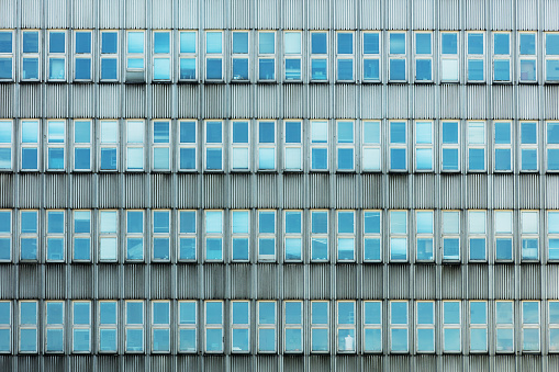 Modern or contemporary facade of a workplace with a pattern of double window and reflection of blue sky. Contemporary office frontal facade with rectangular windows on a modern multinational building