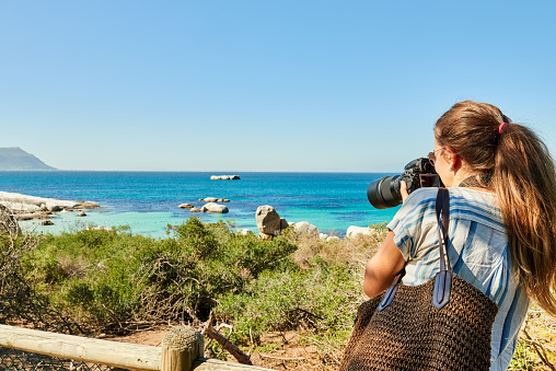 Female tourist standing on a wooden footbridge and taking photos of the scenic view of the beach with a SLR camera