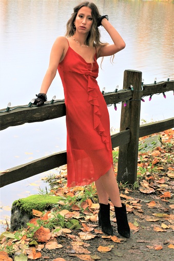 A woman in a red sleeveless dress leaning on a fence in November.