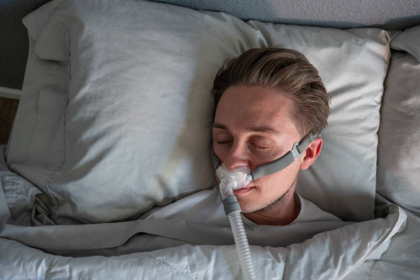 primer plano de un joven con apnea del sueño que usa una máscara cpap en la cama durmiendo de lado - apnea del sueño fotografías e imágenes de stock