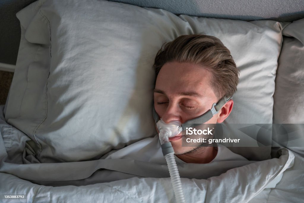 Close Up Of A Young Man With Sleep Apnea Wearing A CPAP Mask In Bed Sleeping On His Side Sleep Apnea Stock Photo