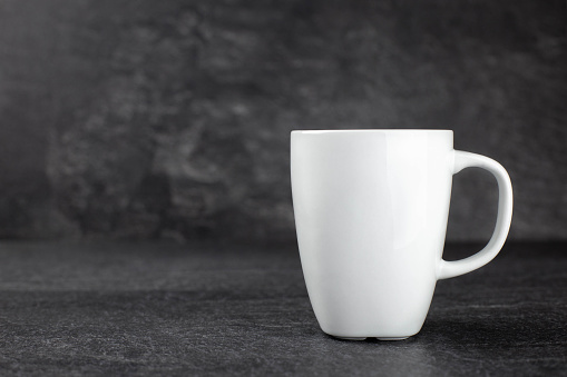 Classic white mug mockup on dark stone background. Side view. Copy space.