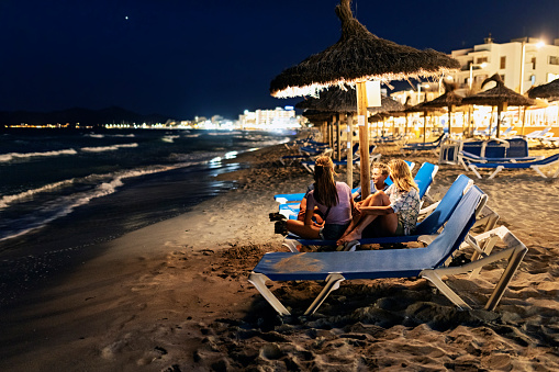 Mother and three kids sitting on beach sunbeds at night. Family is talking and laughing on a warm summer night.
Canon R5