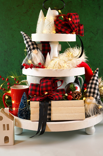 Christmas holiday on-trend Farmhouse aesthetic three tiered tray decor filled with festive decorations, farmhouse style stack of books and gnomes. Vertical orientation.