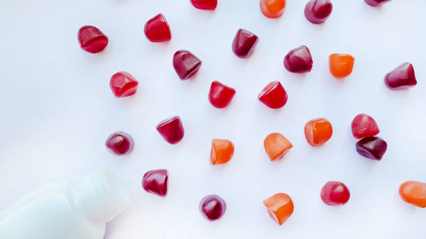 grupo de gomas multivitamínicos vermelhas, laranjas e roxas com a garrafa isolada no fundo branco - gummy - fotografias e filmes do acervo