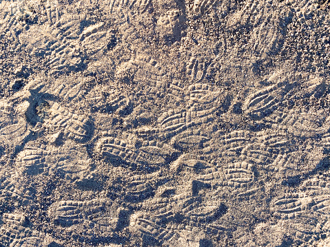 many hiking boot marks and shoe tread prints in the desert trail sand at sunset