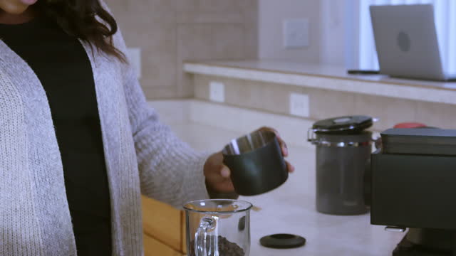 Beautiful Young African-American Woman Grinding Coffee and pouring it into a pour over coffee filter at home