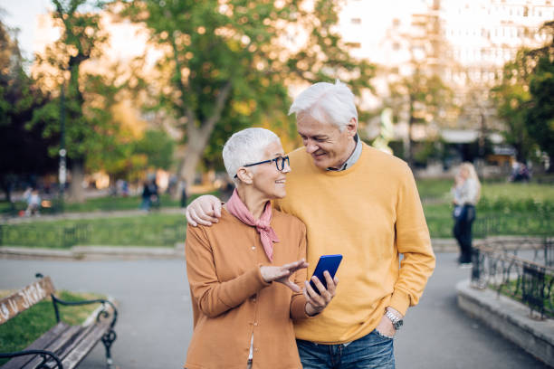 istock Cheerful old couple walking around a public park, using a smart phone 1353896804